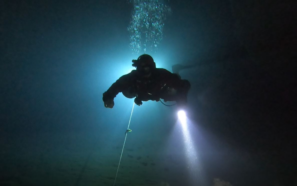 A diver descending into dark water with a light, a guideline below